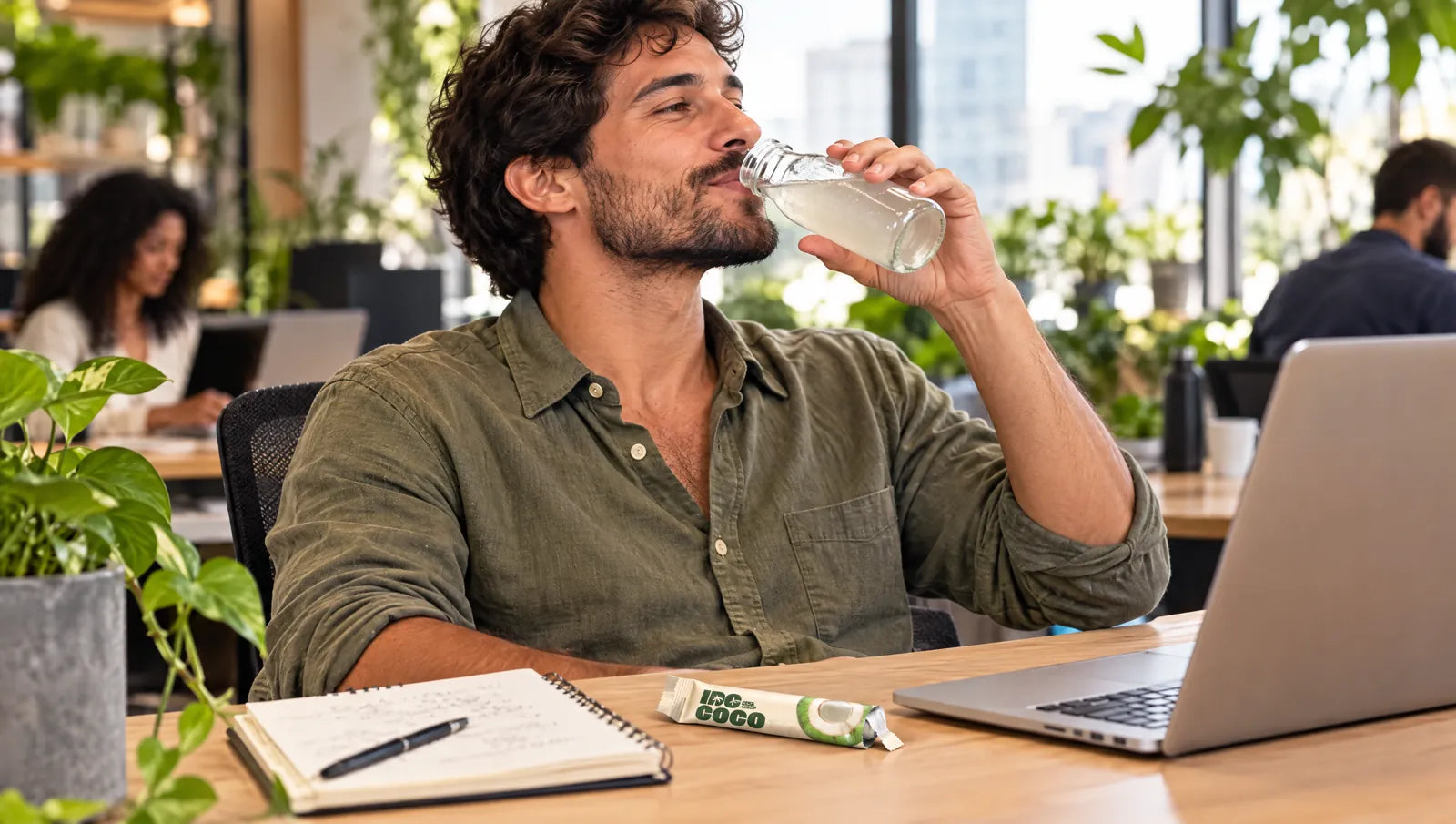 Homme buvant de l'eau de coco à son bureau, un sachet IDCoco à côté de l'ordinateur portable